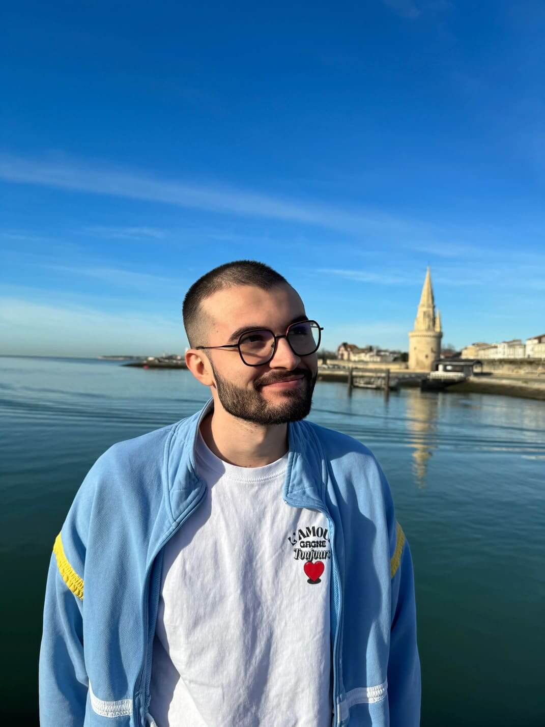 Plan rapproché de Johan Morga, développeur de l’agence WebMarmottes, léger sourire, regard au loin, le port de La Rochelle en arrière plan.