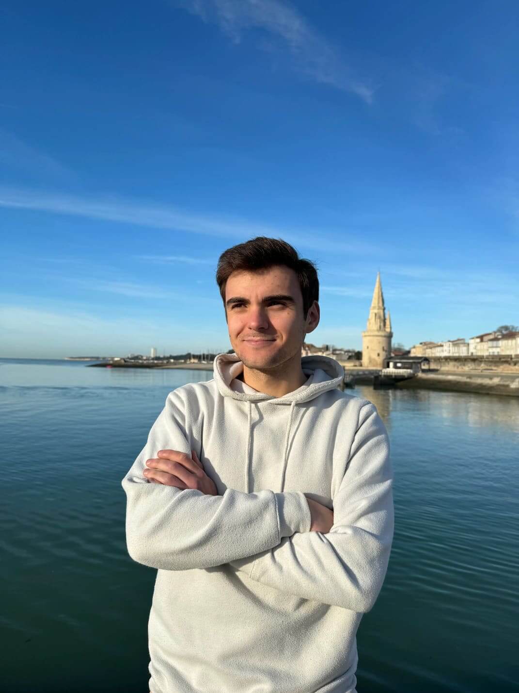 Plan rapproché de Sean Reyboz, développeur de l’agence WebMarmottes, léger sourire, les bras croisés, le port de La Rochelle en arrière plan.