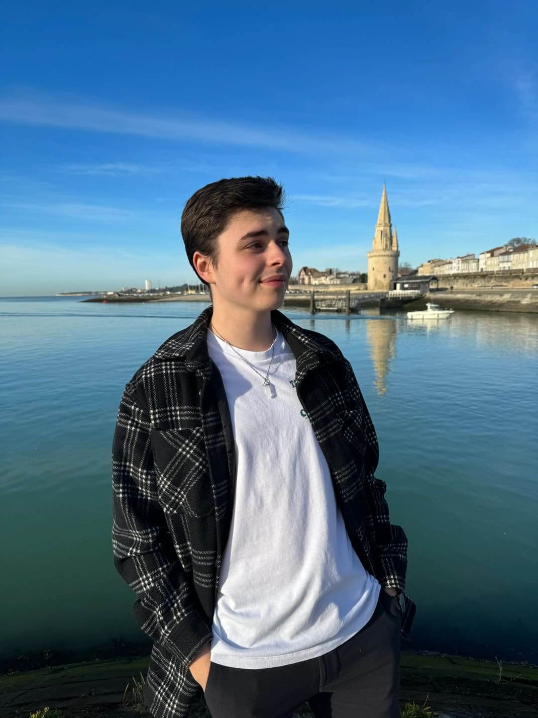 Plan rapproché de Valentin Touzinaud, designer de l’agence WebMarmottes, léger sourire, regard au loin, le port de La Rochelle en arrière plan.